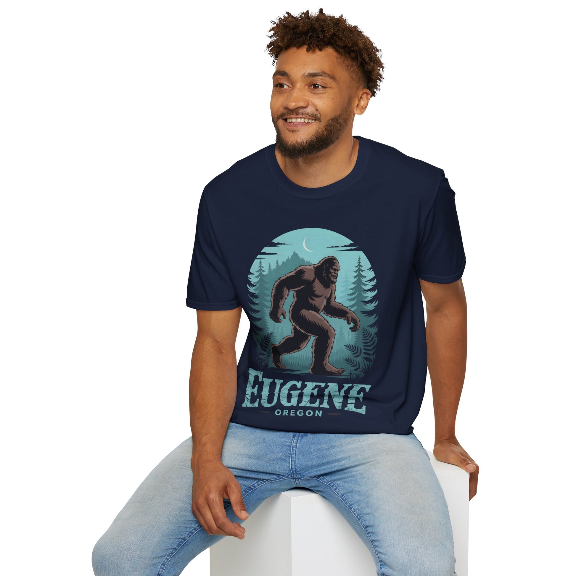 Model wearing a navy Eugene Oregon Bigfoot Tshirt with a large Bigfoot walking through a moonlit forest design, featuring teal pine trees and Eugene Oregon text on the front.