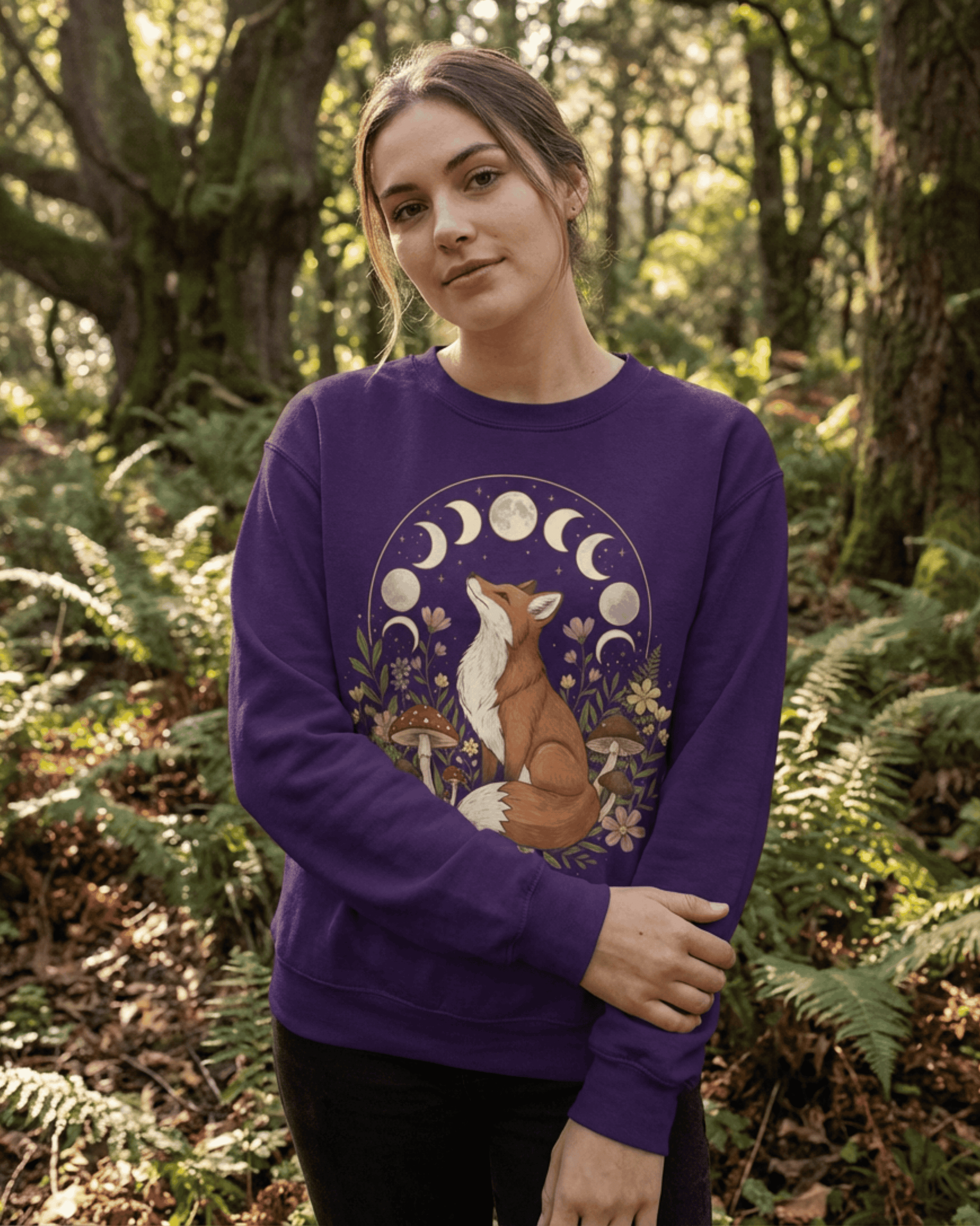Model in woodland clearing wearing purple cottagecore fox sweatshirt with moon phases, mushrooms and wildflowers.