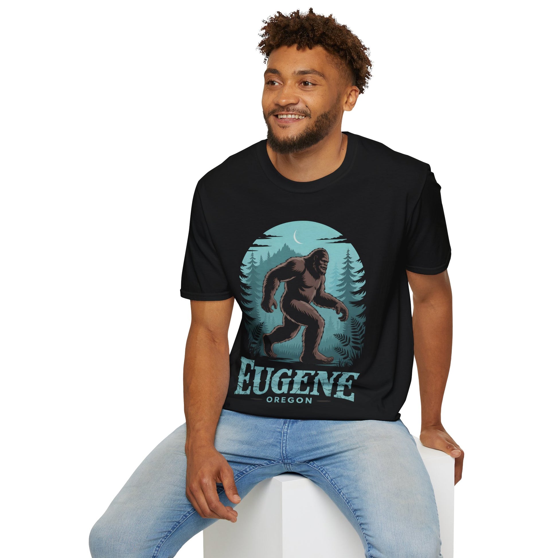 Model wearing a black Eugene Oregon Bigfoot Tshirt with a large Bigfoot walking through a moonlit forest design, featuring teal pine trees and Eugene Oregon text on the front.