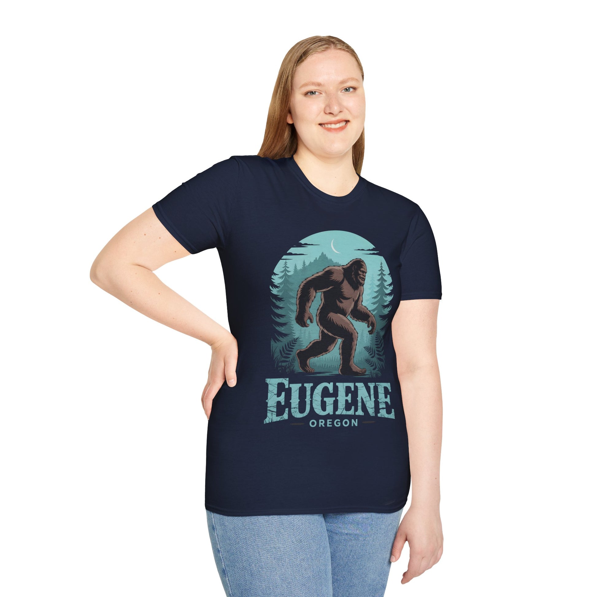 Eugene Oregon Bigfoot Tshirt shown on smiling model, navy tee with teal forest, crescent moon and walking sasquatch graphic, styled with light blue jeans.

