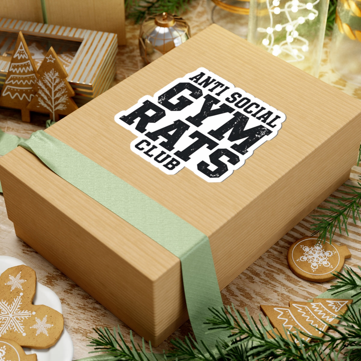 Gift box with a 'Anti Social Gym Rats Club' sticker placed on top. Festive decor in the background. 