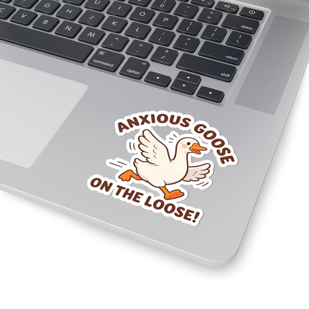 A kiss-cut vinyl sticker featuring a cartoon white goose with orange beak and feet, surrounded by the text 'ANXIOUS GOOSE ON THE LOOSE!' in brown, shown applied to the palm rest of a silver laptop.