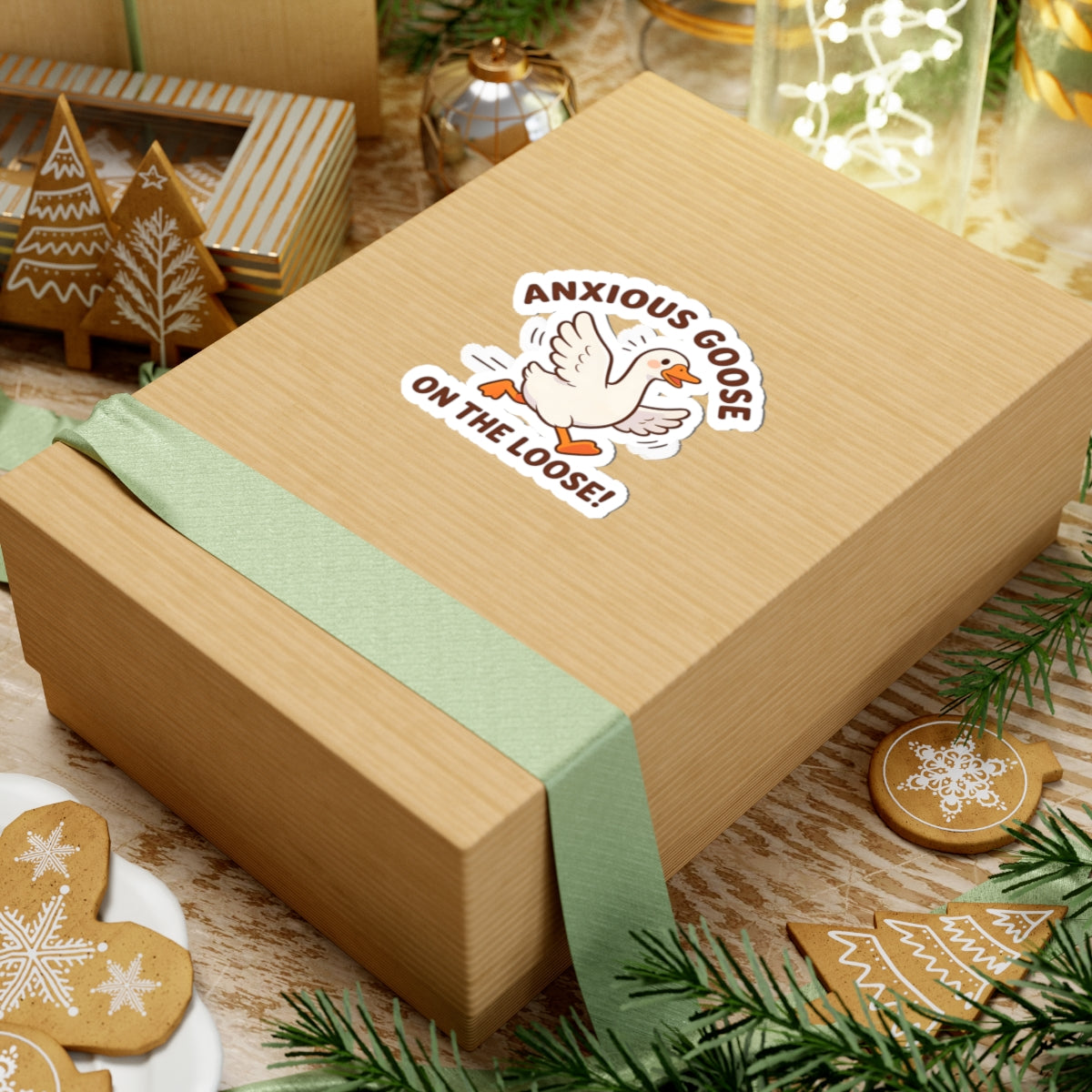 Gift box with a green ribbon with a cute goose sticker with the text 'ANXIOUS GOOSE ON THE LOOSE!' on a festive background with cookies and decorations.