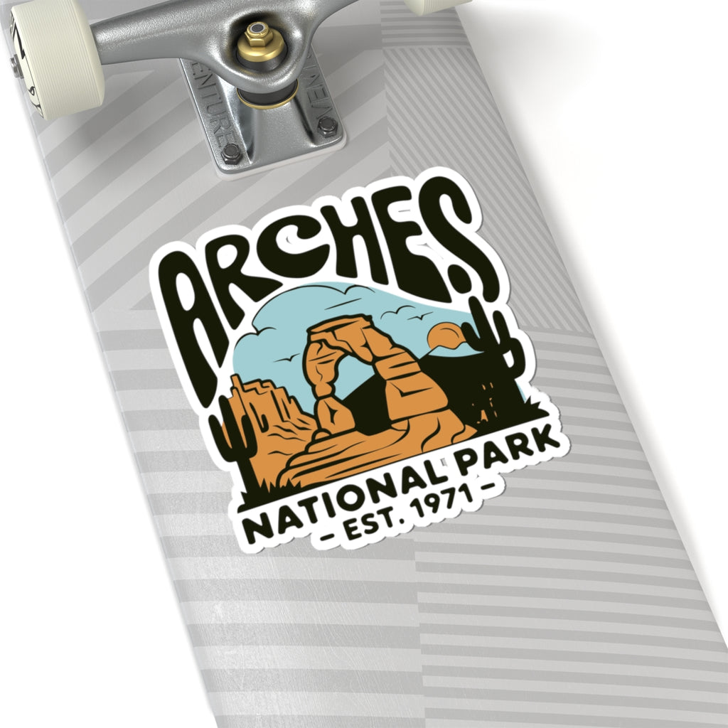 A close-up of a skateboard deck featuring a kiss-cut sticker that reads 'ARCHES NATIONAL PARK - EST. 1971' with a desert arch illustration.