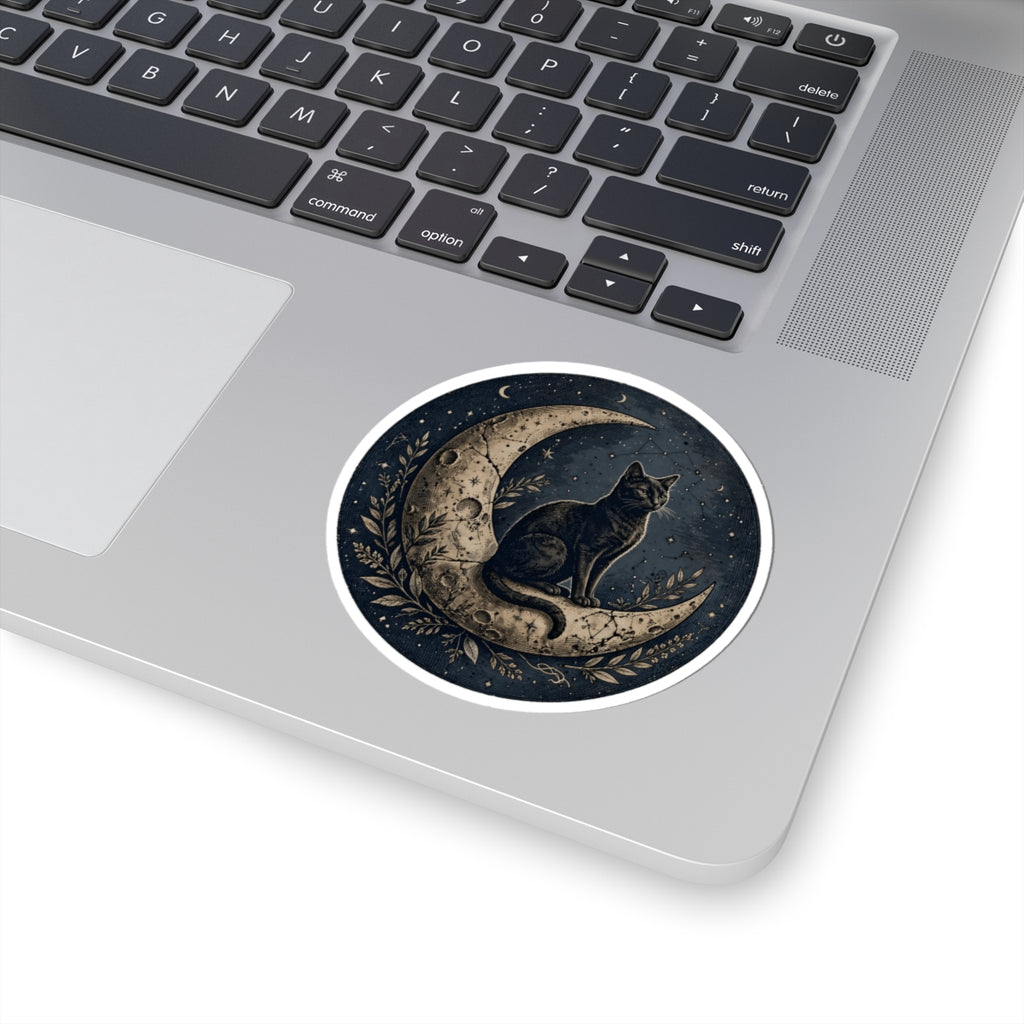 A round sticker featuring a black cat sitting on a crescent moon, applied to the palm rest of a silver laptop. The sticker has a white border and is shown against a clean white background.