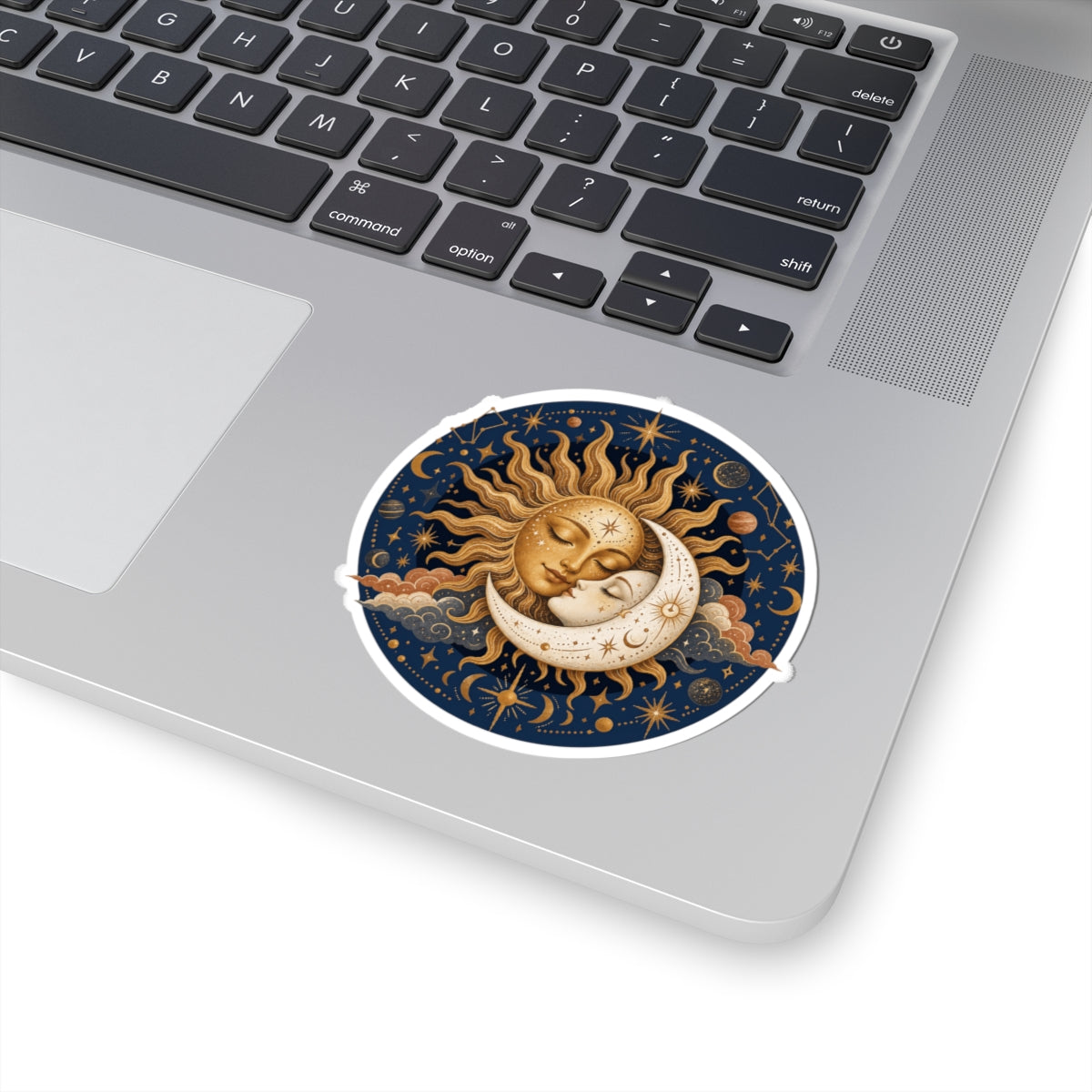 A round sticker with a celestial design of a sleeping sun and crescent moon on a dark blue starry background, shown applied to the palm rest of a silver laptop.