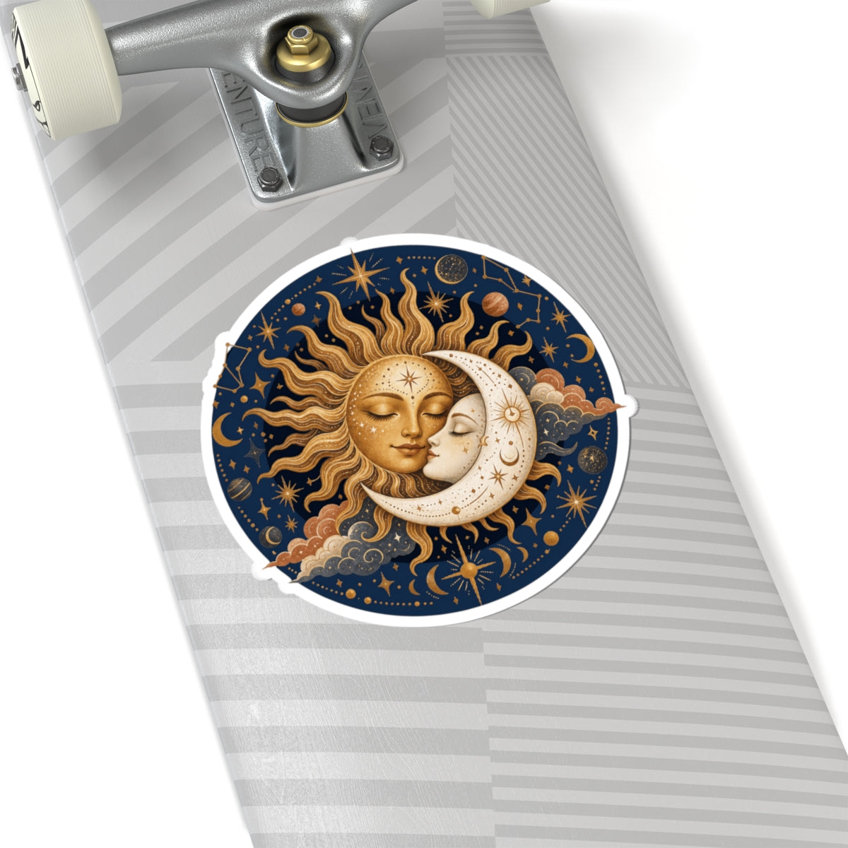 A circular sticker with a celestial design of a kissing sun and moon, shown applied to the side of a skateboard deck.