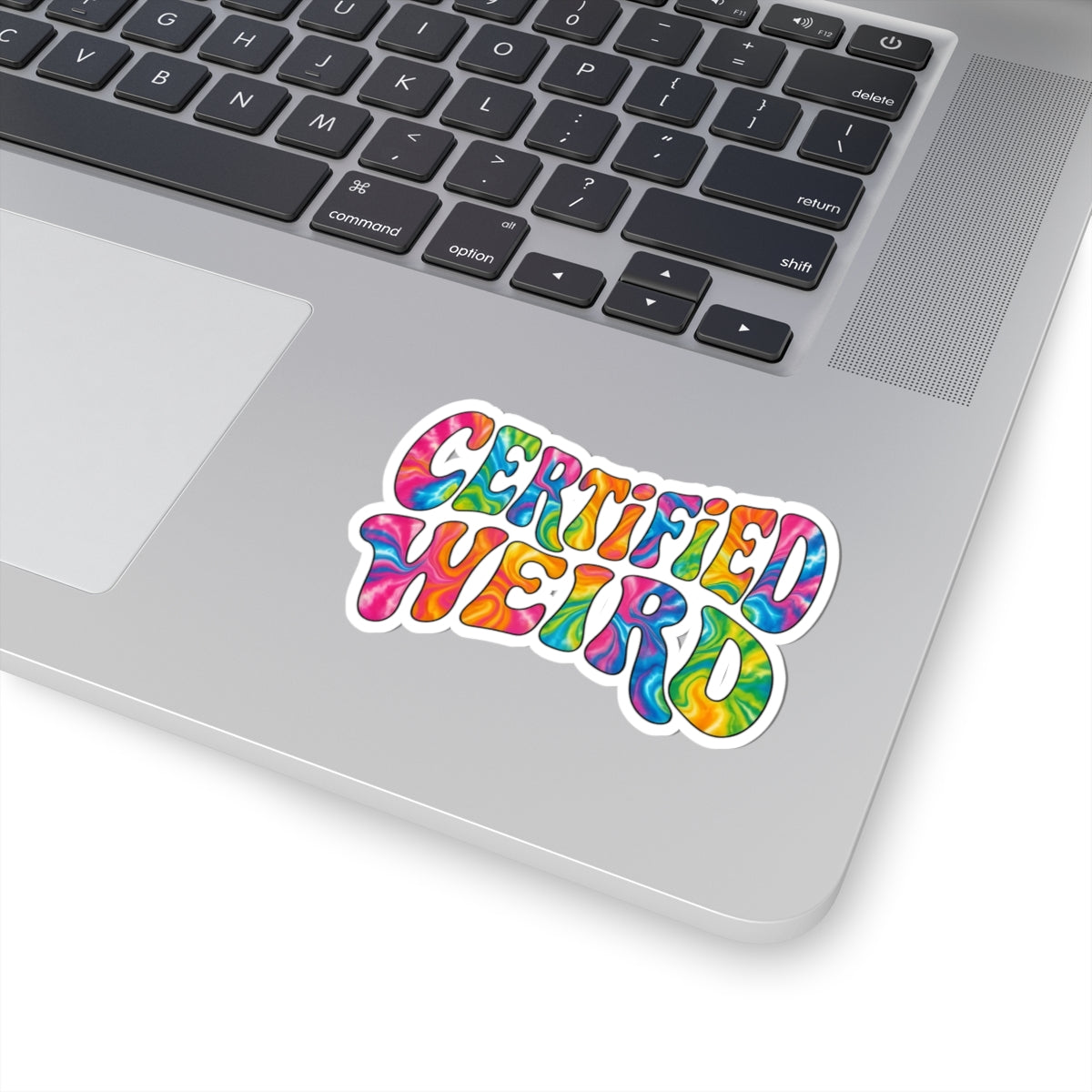 A colorful kiss-cut sticker reading 'CERTIFIED WEIRD' in rainbow tie-dye lettering, shown applied to the palm rest of a silver laptop on a white background.