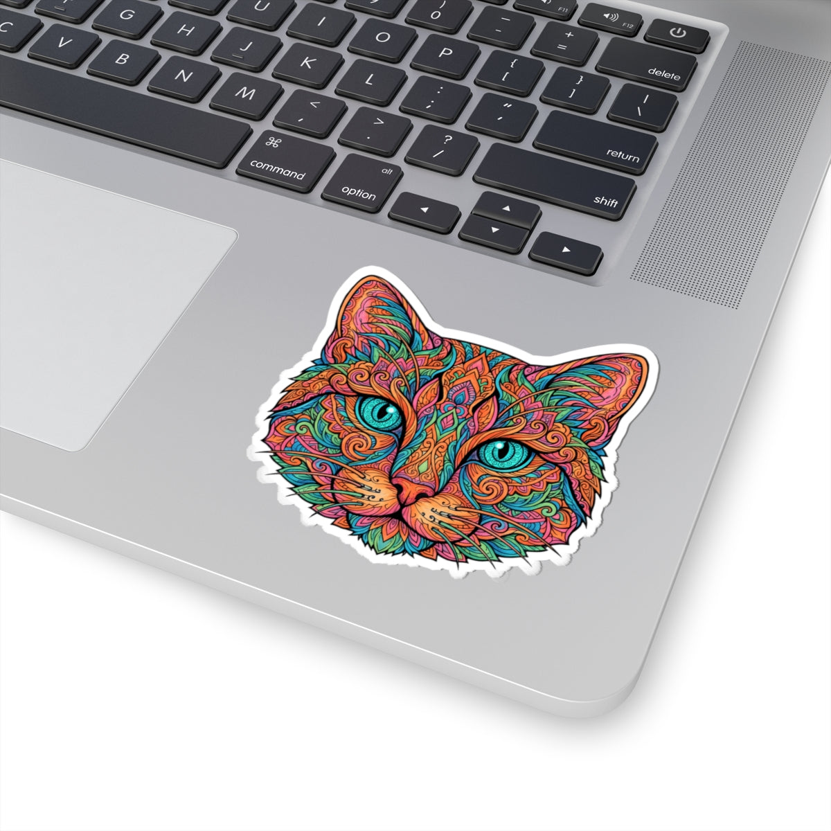 A kiss-cut vinyl sticker of a colorful, patterned cat face applied to the silver surface of a laptop keyboard.