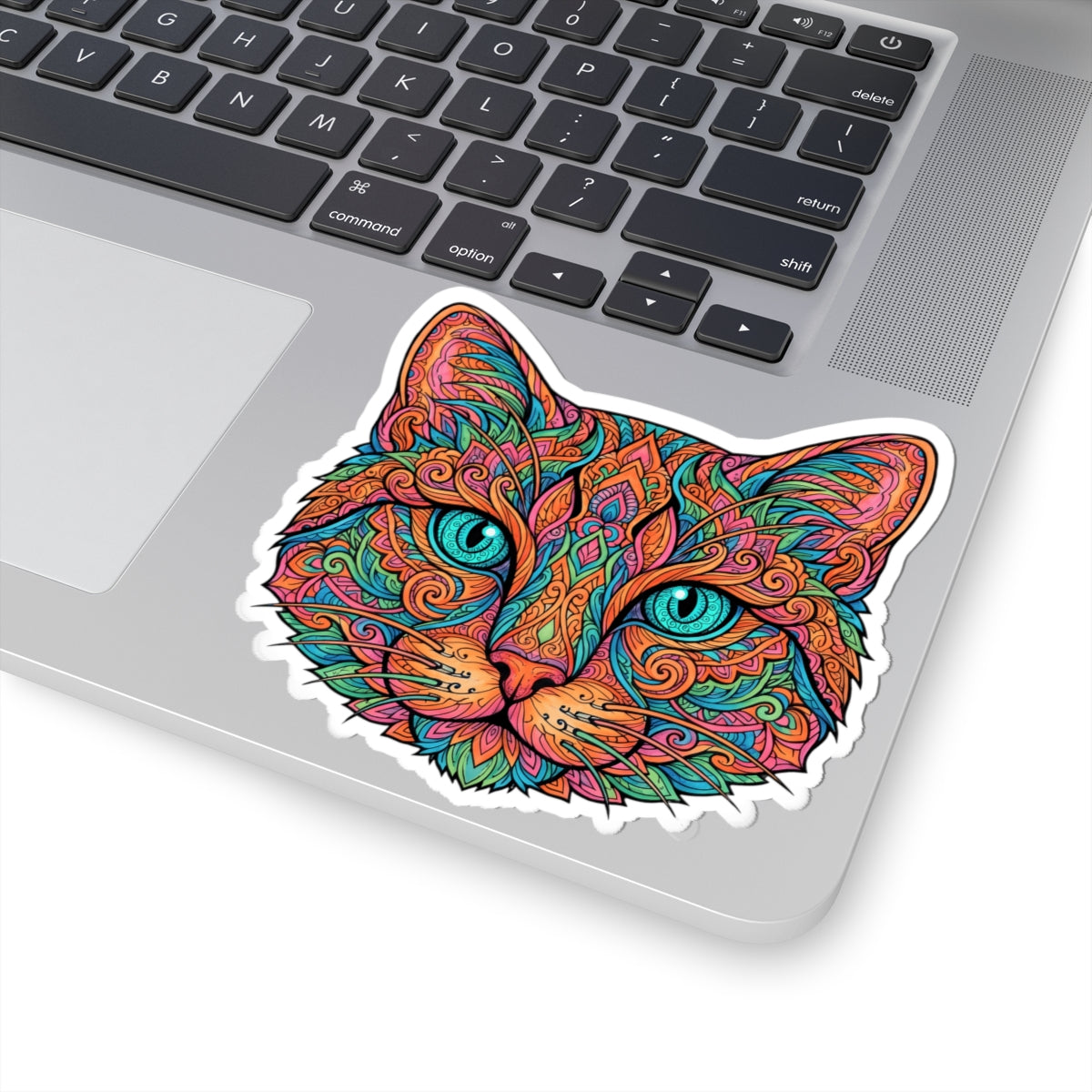 A kiss-cut vinyl sticker of a colorful, psychedelic cat face with turquoise eyes, shown applied to the silver surface of a laptop keyboard.