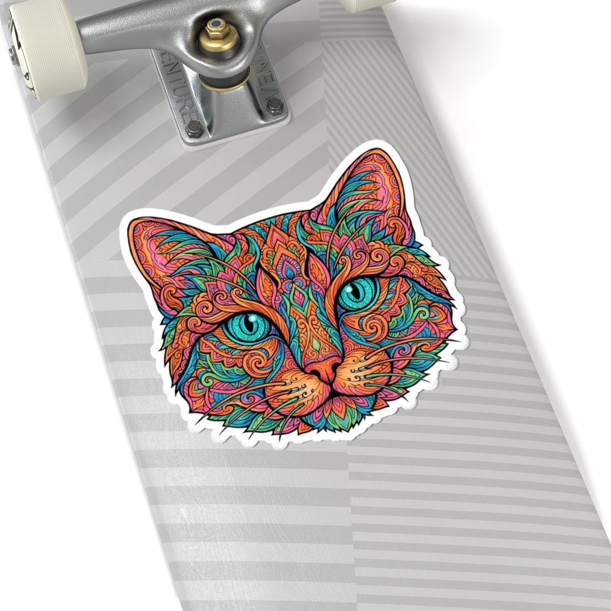 A colorful cat-face sticker with intricate mandala-style patterns and bright turquoise eyes, shown applied to the underside of a silver skateboard.