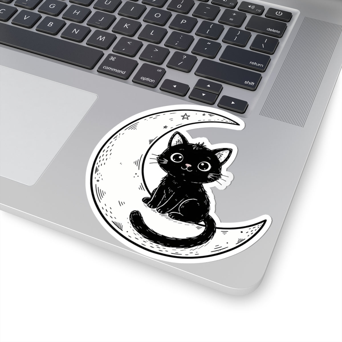 A kiss-cut vinyl sticker of a cute black cat sitting on a crescent moon, shown applied to the corner of a silver laptop.