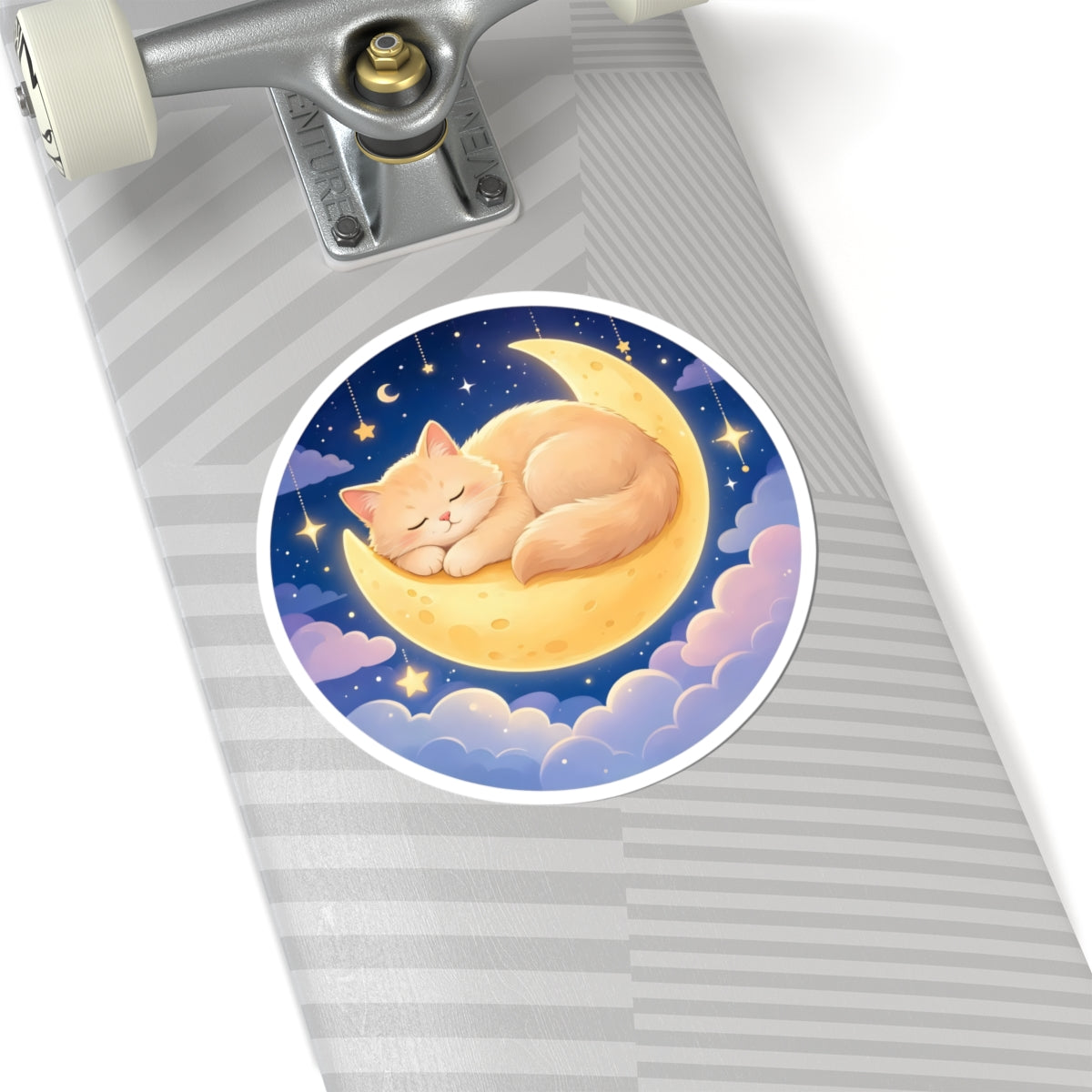 A round sticker featuring a sleeping orange cat curled up on a crescent moon under a starry night sky, shown applied to the deck of a skateboard.
