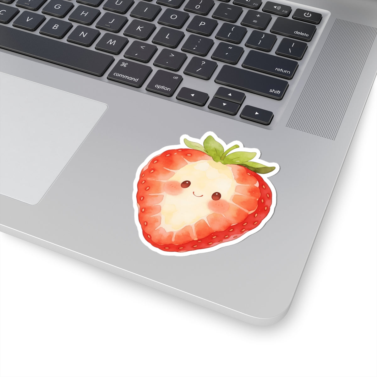 A kiss-cut vinyl sticker of a cute, smiling strawberry with green leaves, shown applied to the palm rest of a silver laptop.