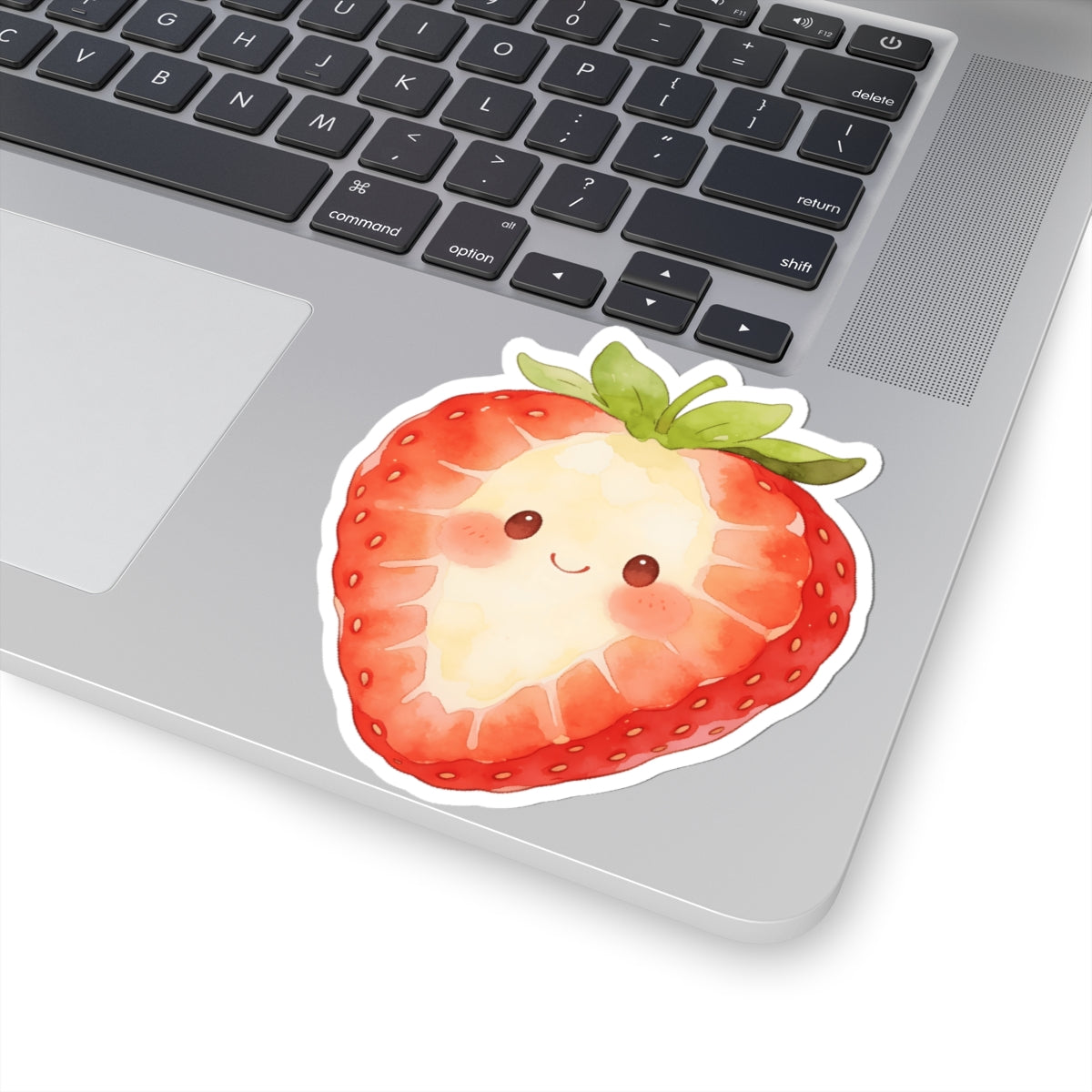 A kiss-cut sticker of a cute, smiling watercolor strawberry with green leaves, shown applied to the corner of a silver laptop.