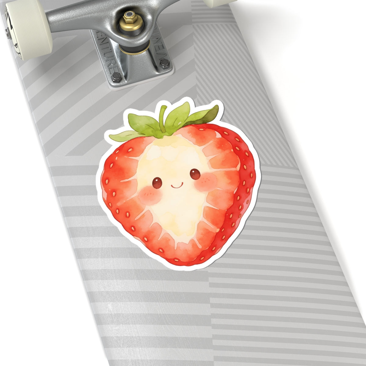 A kiss-cut sticker of a cute, smiling strawberry with green leaves, shown applied to the striped gray and white surface of a skateboard deck near the truck.