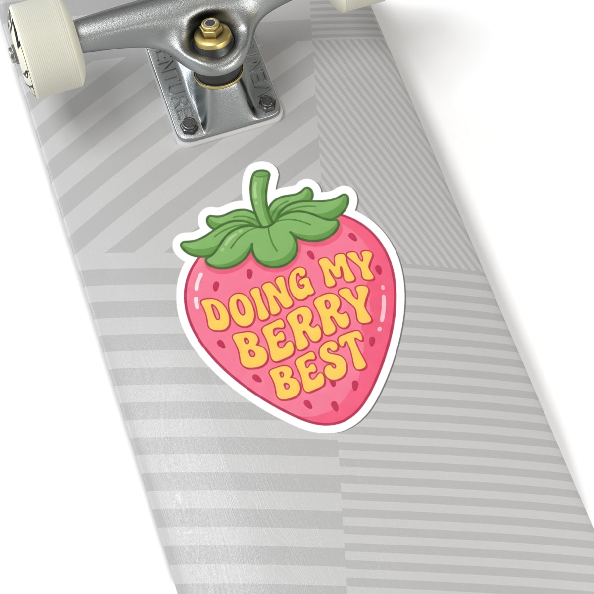 A kiss-cut sticker shaped like a strawberry with the text 'DOING MY BERRY BEST' in yellow, placed on a gray striped skateboard deck. The sticker has a pink body with a green leafy top and a white outline.