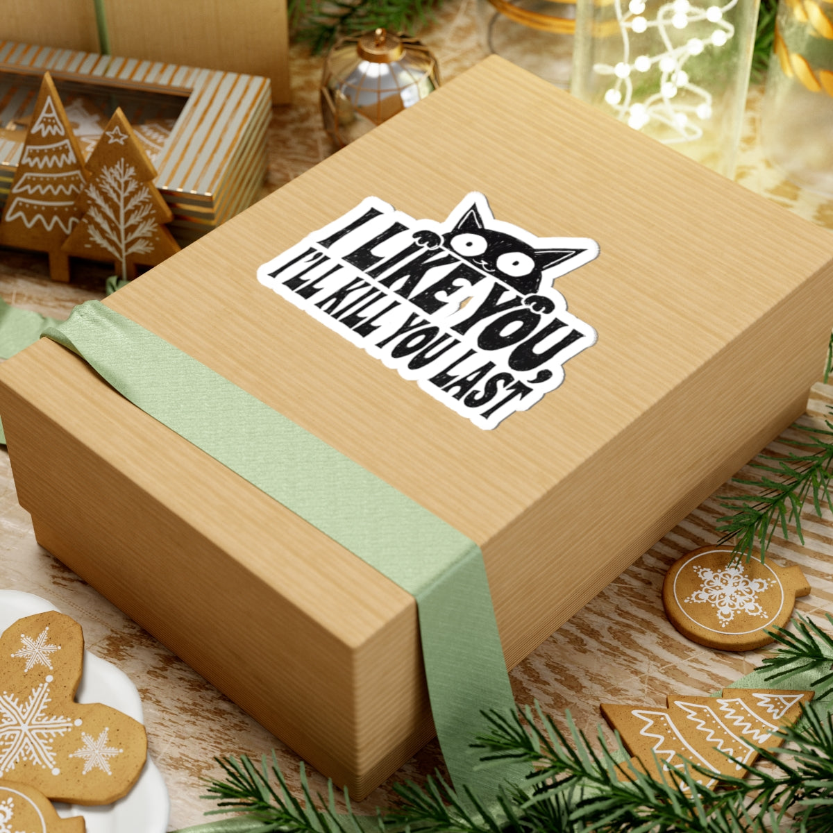 Wooden gift box with a green ribbon and 'Tattoo Studio' sticker featuring a cartoon black cat and text 'I LIKE YOU, I'LL KILL YOU LAST' on a festive background.