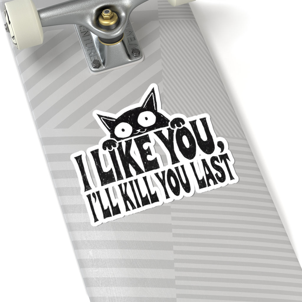 A kiss-cut vinyl sticker applied to the underside of a skateboard deck. The sticker features a black cartoon cat peeking over bold black text that reads 'I LIKE YOU, I'LL KILL YOU LAST' on a white background with a gray striped skateboard deck.