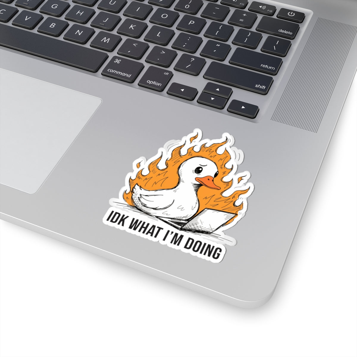 A kiss-cut vinyl sticker applied to the lower right corner of a silver laptop. The sticker features a cartoon white duck surrounded by orange flames, with the text 'IDK WHAT I'M DOING' in black capital letters below.