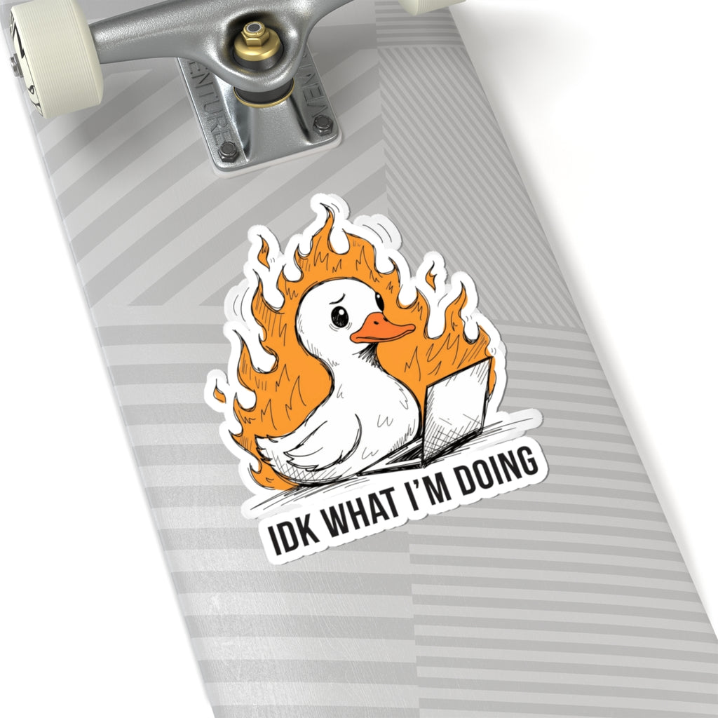 A kiss-cut sticker featuring a white duck surrounded by orange flames and a laptop, with the text 'IDK WHAT I'M DOING', shown applied to the underside of a gray striped skateboard near the trucks.