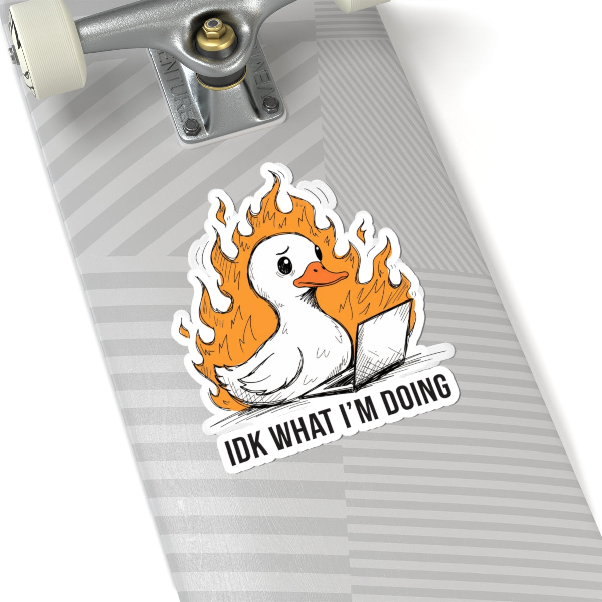 A kiss-cut sticker featuring a white duck surrounded by orange flames and a laptop, with the text 'IDK WHAT I'M DOING', shown applied to the underside of a gray striped skateboard near the trucks.