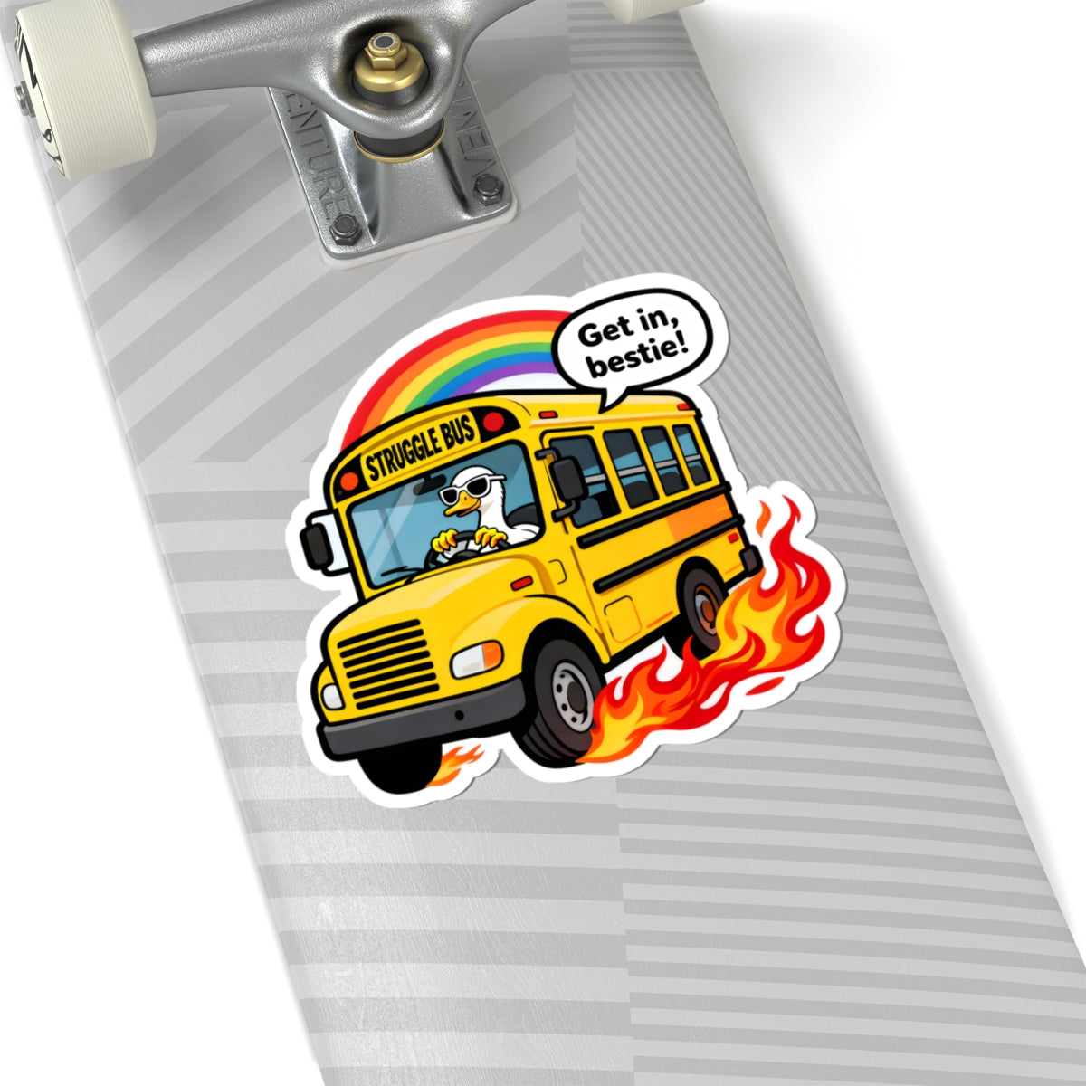 A kiss-cut sticker featuring a yellow school bus with flames, a rainbow, and a speech bubble that says 'Get in, bestie!' applied to a gray striped skateboard deck.