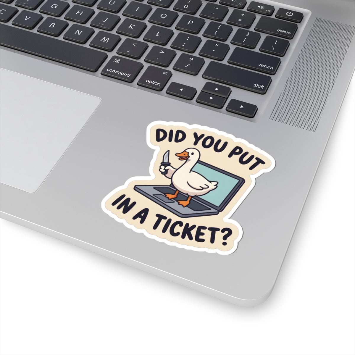 A kiss-cut vinyl sticker featuring a cartoon white duck holding a keyboard and a knife, with the text 'DID YOU PUT IN A TICKET?' in black letters on a beige background. The sticker is shown applied to the palm rest of a silver laptop.