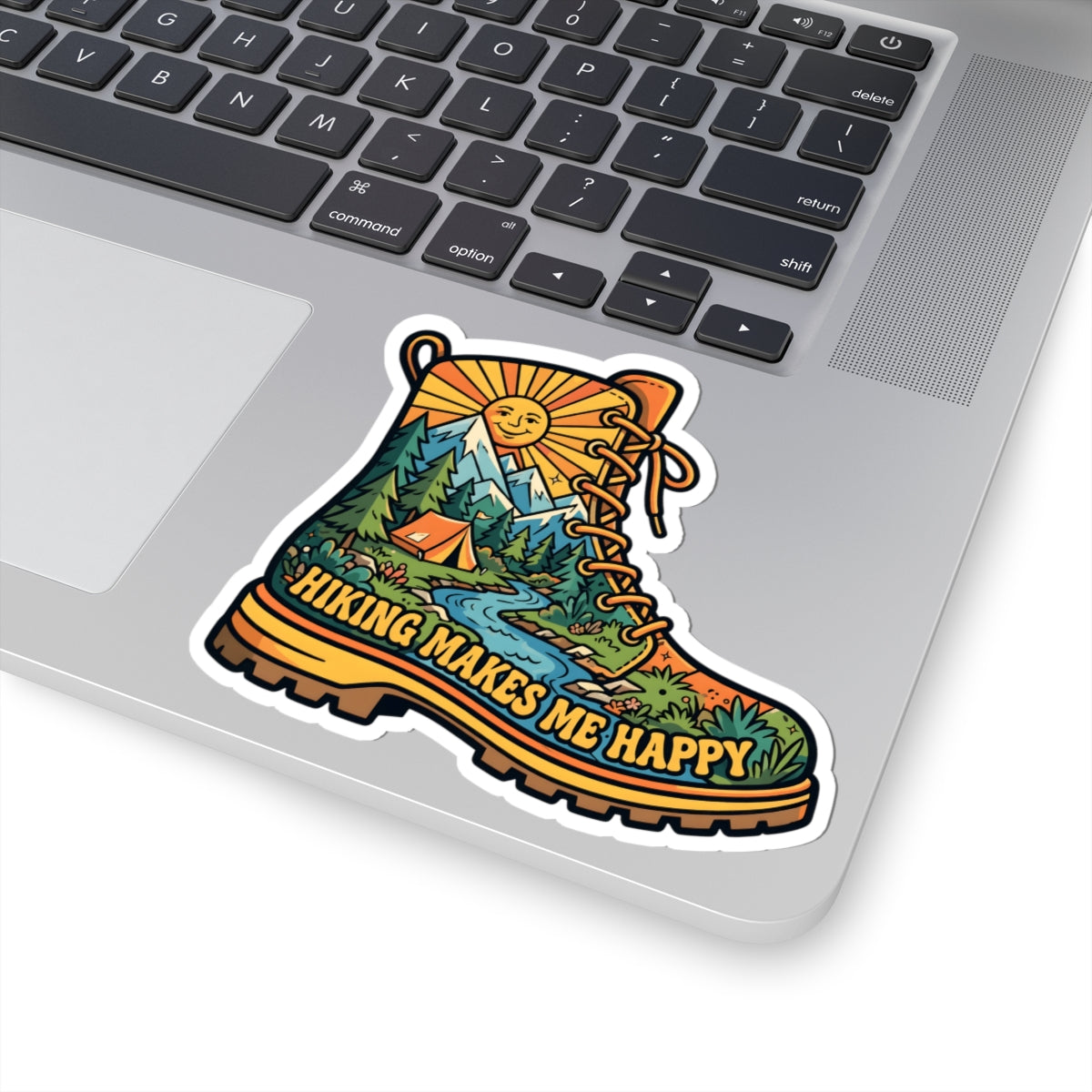 A kiss-cut vinyl sticker of a hiking boot with a scenic landscape and the text 'HIKING MAKES ME HAPPY' displayed on a silver laptop.
