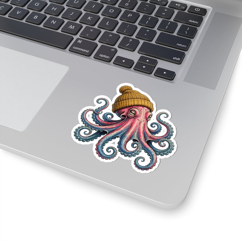 A kiss-cut vinyl sticker of an octopus wearing a knit beanie, shown applied to the silver palm rest of a laptop keyboard.