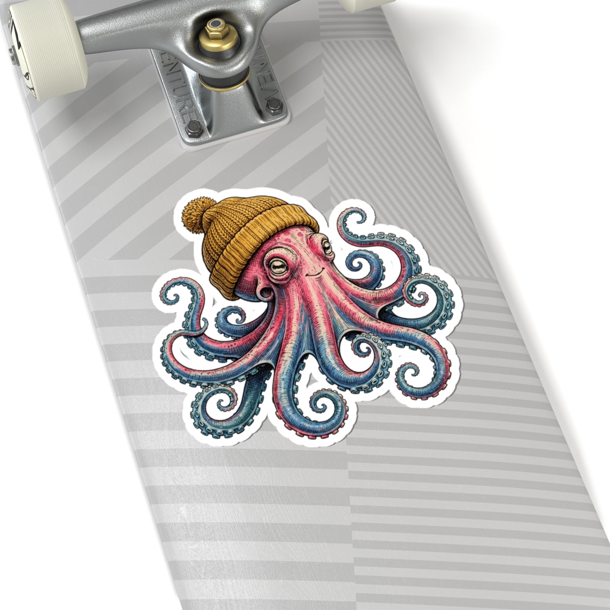 A kiss-cut vinyl sticker of a cute pink octopus wearing a yellow knit beanie, shown applied to the deck of a skateboard with a gray and white striped pattern.