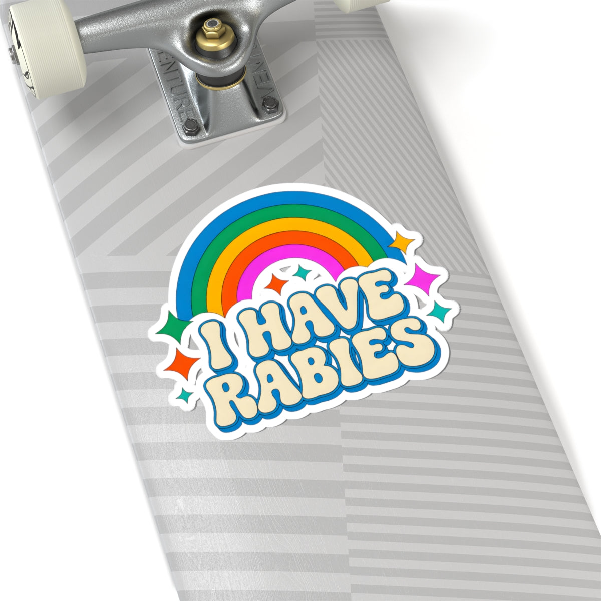 A kiss-cut vinyl sticker reading 'I HAVE RABIES' in a playful retro font, featuring a rainbow and stars, shown applied to the deck of a skateboard.