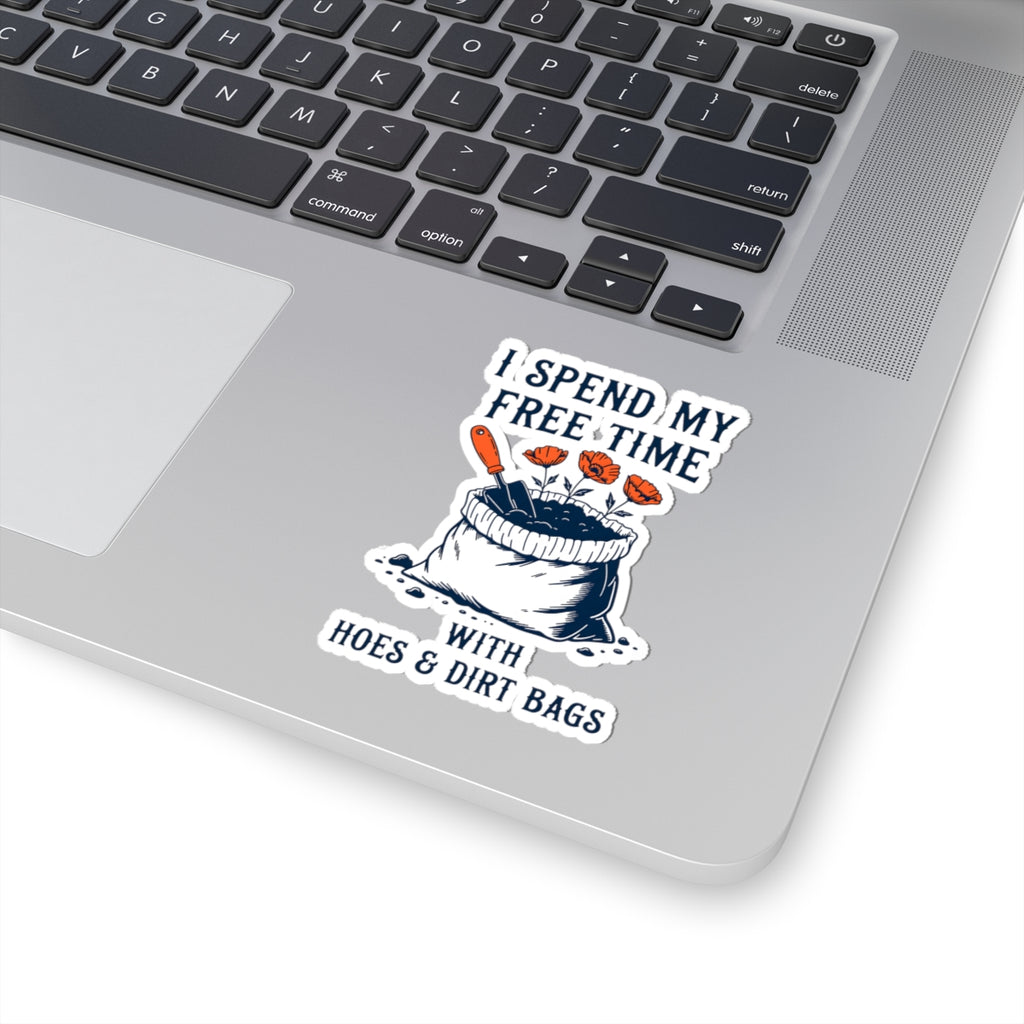 A kiss-cut vinyl sticker applied to the lower right corner of a silver laptop. The sticker features a cartoon illustration of garden supplies, with the text 'I SPEND MY FREE TIME WITH HOES & DIRT BAGS'.