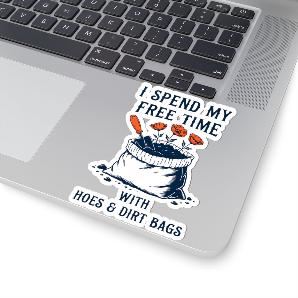 A kiss-cut vinyl sticker applied to the corner of a silver laptop. The sticker features a humorous graphic with the text 'I SPEND MY FREE TIME WITH HOES & DIRT BAGS' surrounding an illustration of a black-and-white bag of dirt with orange gardening tools and flowers.