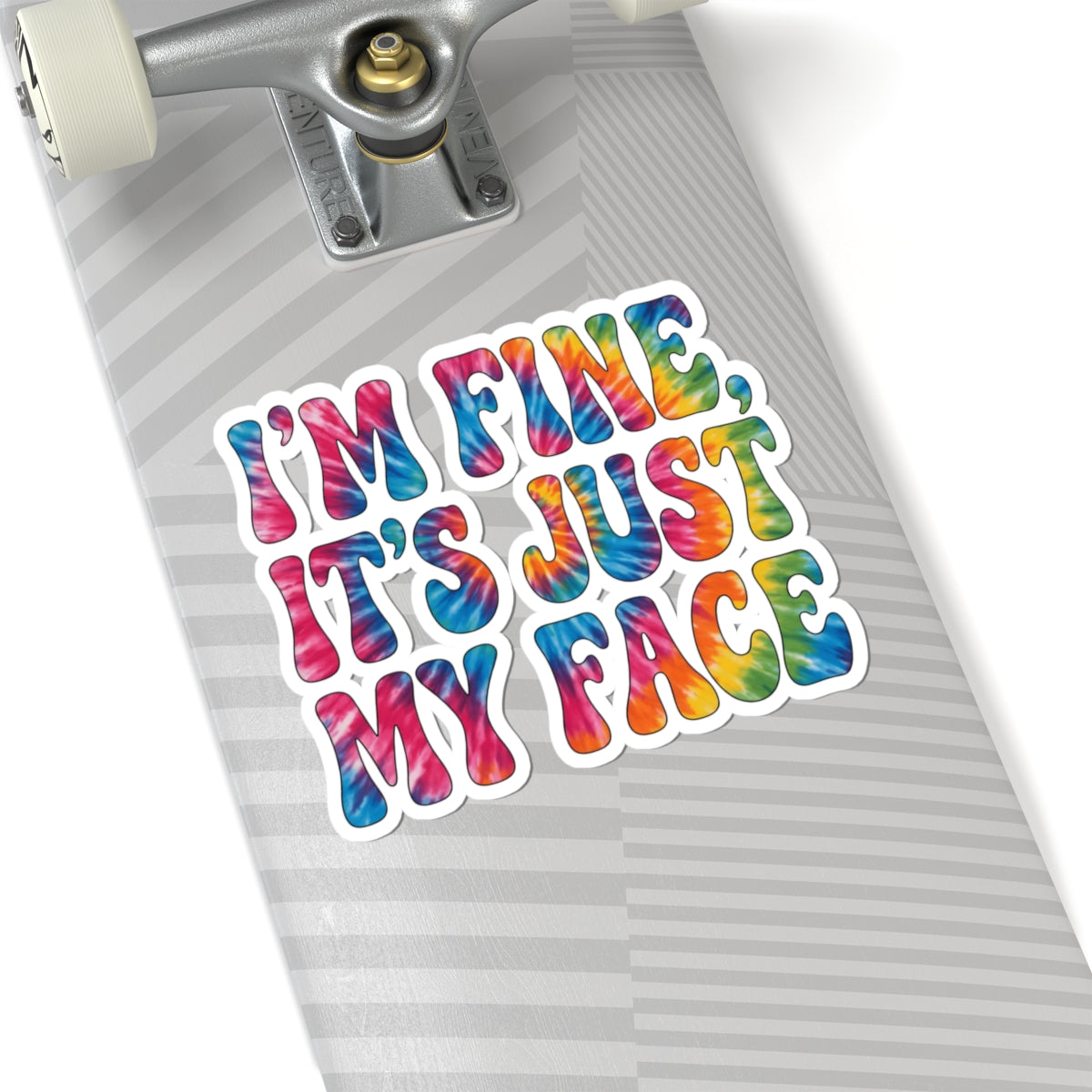A kiss-cut vinyl sticker with the text 'I'M FINE, IT'S JUST MY FACE' in a colorful tie-dye pattern, shown applied to the deck of a skateboard.