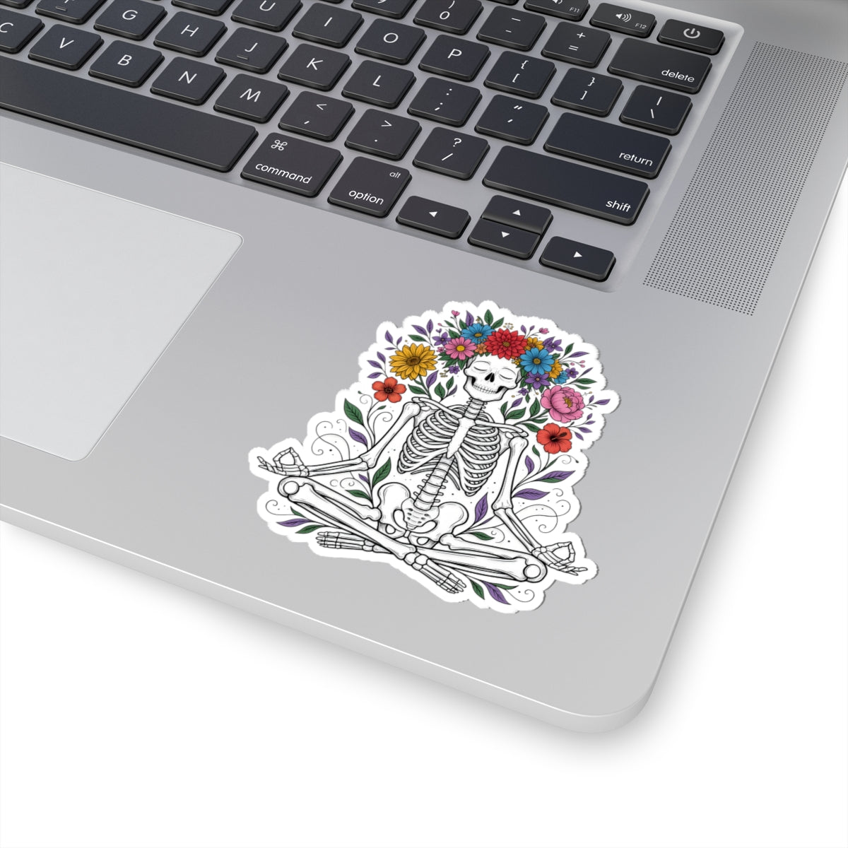 Laptop with a line art skeleton sticker wearing a floral crown shown on the palm of the laptop. 