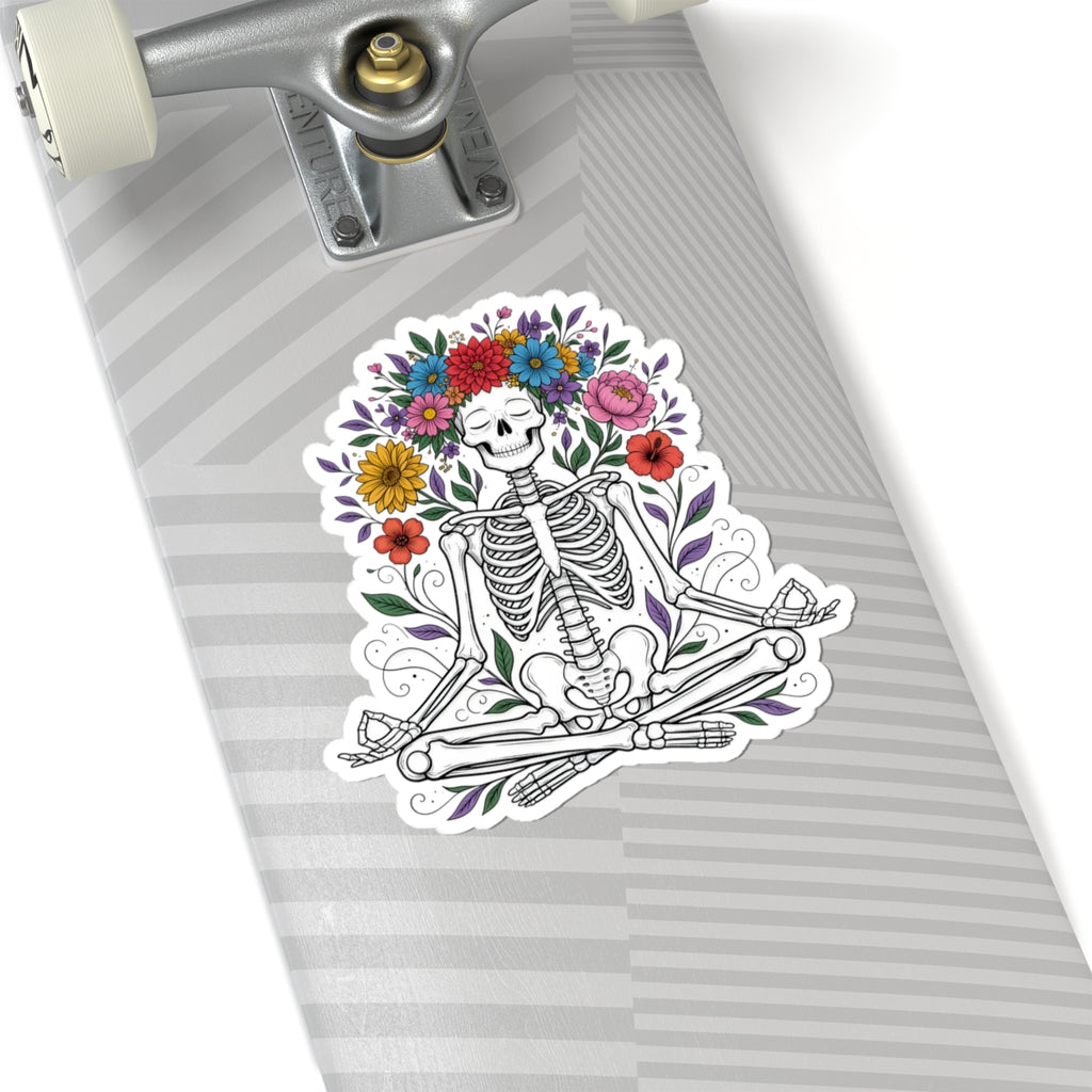A kiss-cut sticker featuring a Day of the Dead skeleton sitting cross-legged under a colorful flower crown, shown applied to the deck of a skateboard.