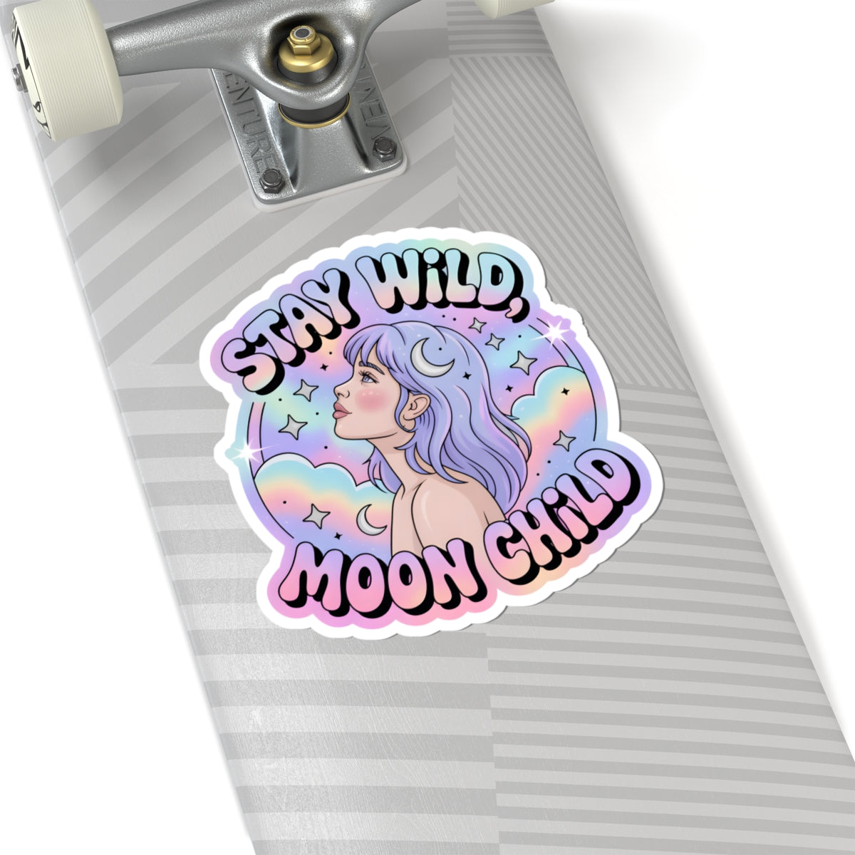A kiss-cut sticker with the text 'STAY WILD, MOON CHILD' in black outlined lettering, featuring an illustration of a woman with purple hair and a crescent moon, shown on a gray striped skateboard deck.