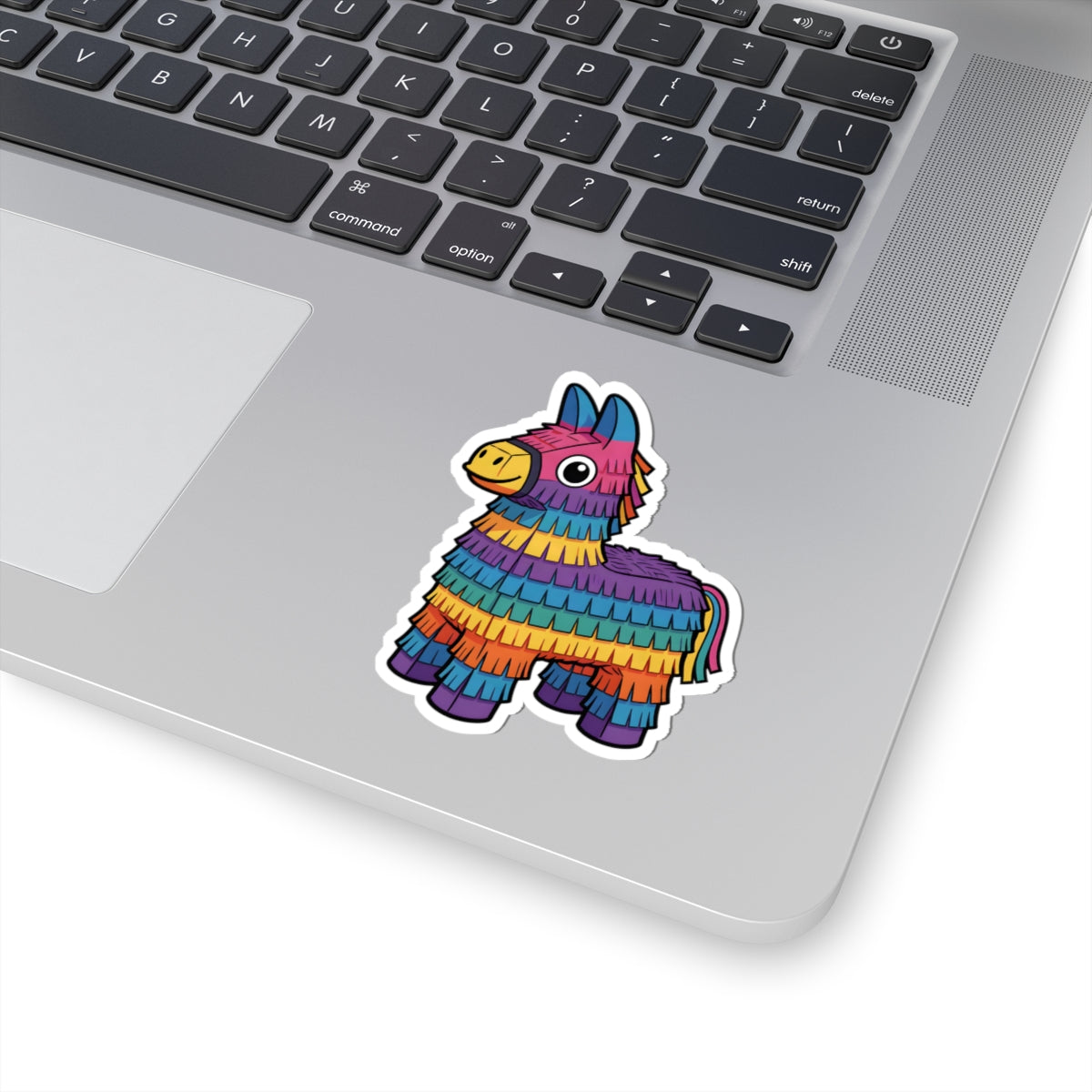 A colorful piñata llama sticker applied to the silver palm rest of a laptop keyboard, shown on a clean white background.