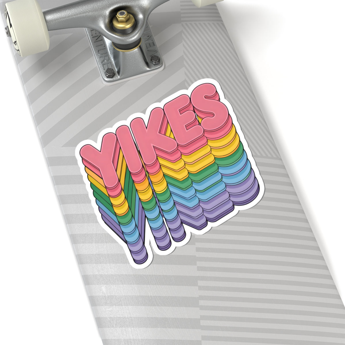 A kiss-cut vinyl sticker featuring the word 'YIKES' in pink 3D letters with a rainbow-striped shadow effect, shown applied to the deck of a skateboard.