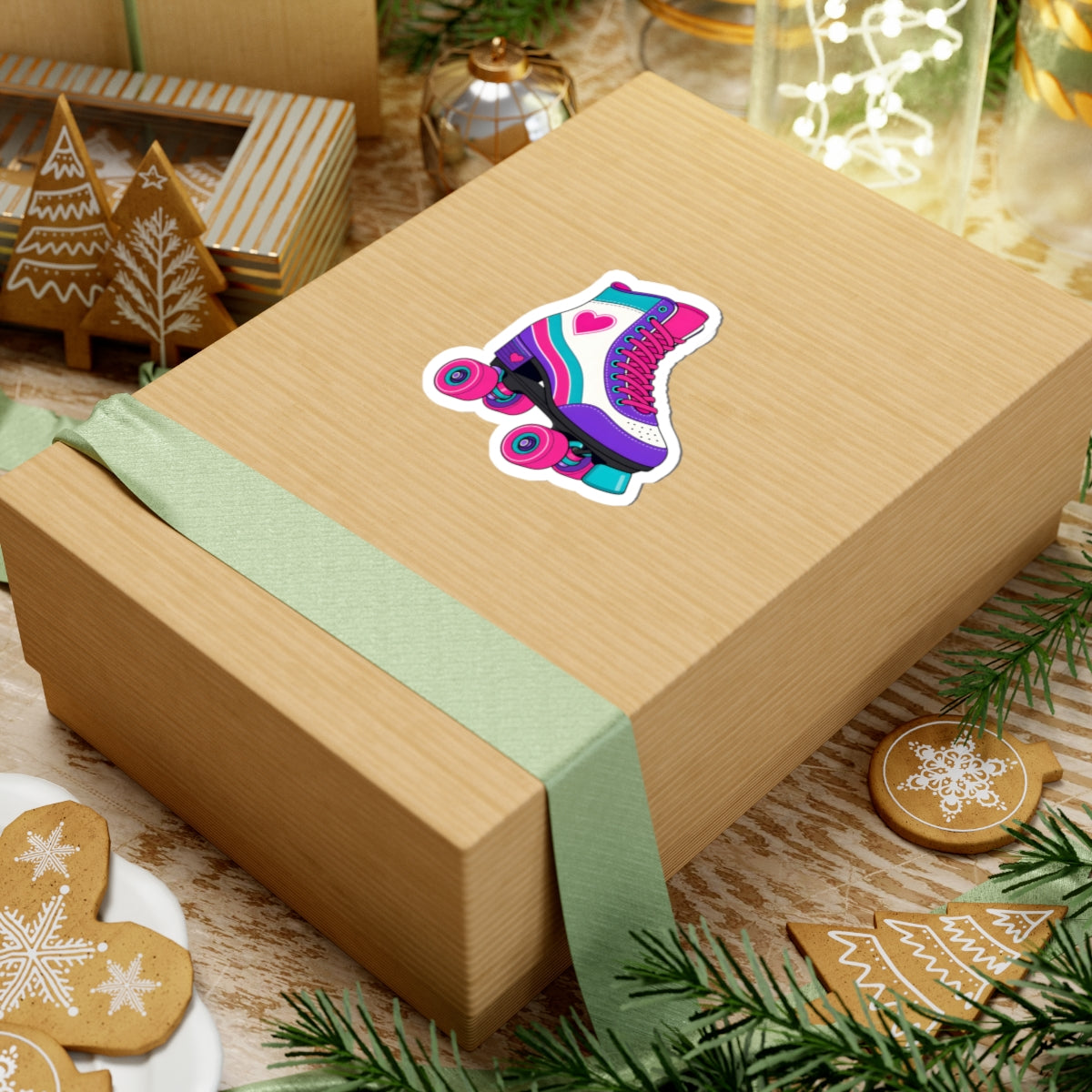 A kraft paper gift box wrapped with a pale green ribbon, featuring a colorful roller skate sticker on top, styled with holiday cookies, pine branches, and other gift boxes.