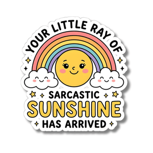 A kiss-cut sticker featuring a cute cartoon design with a smiling yellow sun, rainbow, clouds, and stars. The text reads 'YOUR LITTLE RAY OF SARCASTIC SUNSHINE HAS ARRIVED' on a white background with a soft drop shadow.