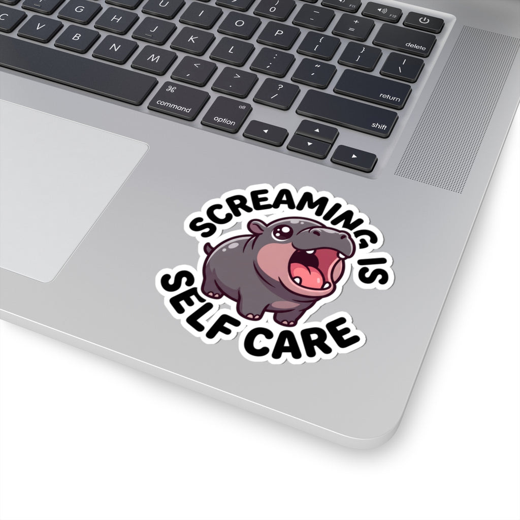 A kiss-cut vinyl sticker featuring a cartoon hippopotamus and the text 'SCREAMING IS SELF CARE' applied to the palm rest of a silver laptop.