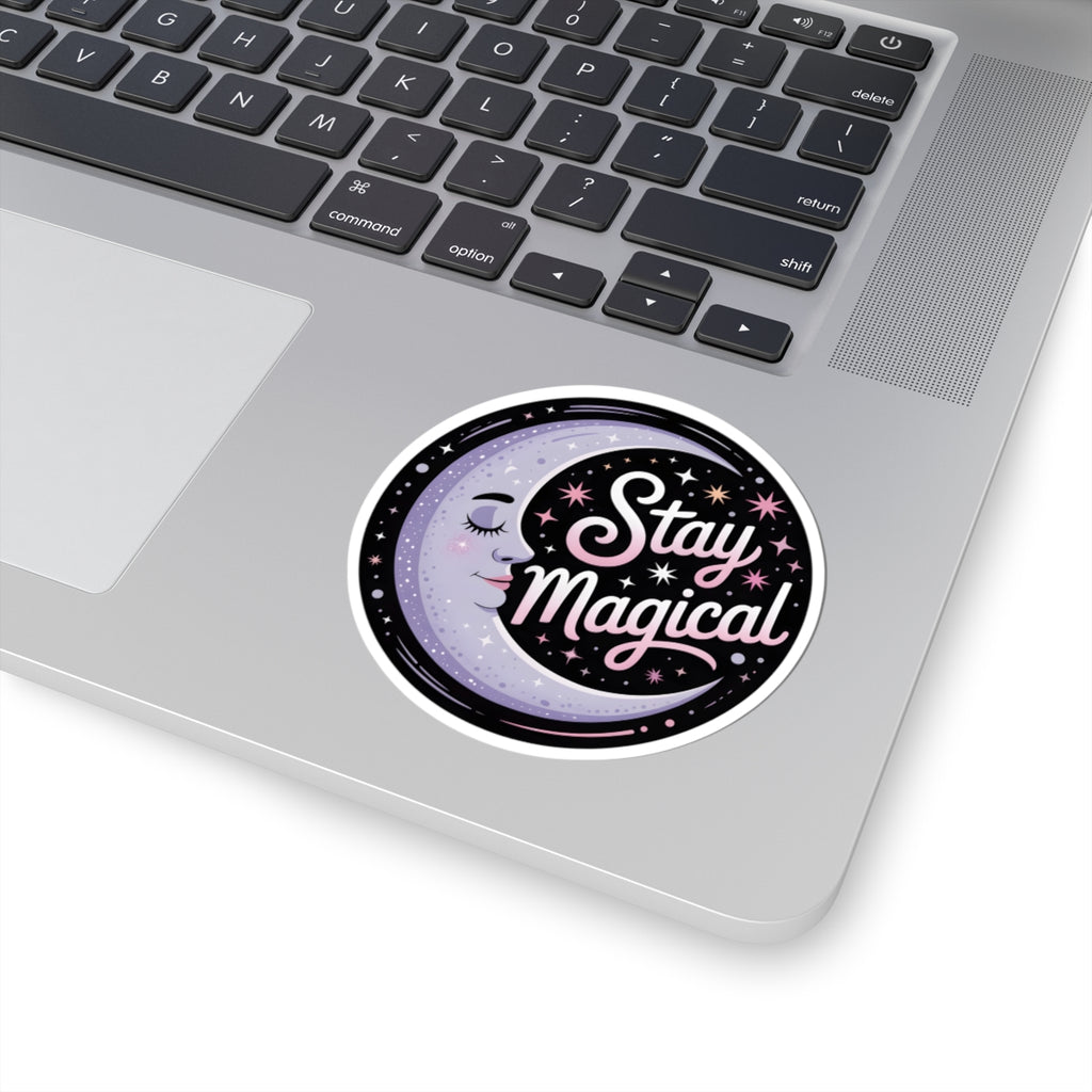 A round vinyl sticker with the words 'Stay Magical' in pink script over a purple moon and black starry background, shown applied to the palm rest of a silver laptop.