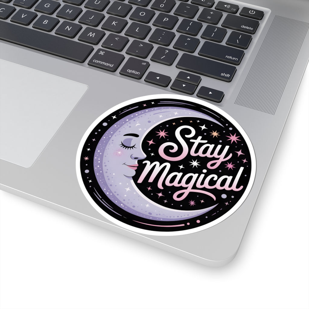 A round vinyl sticker with the phrase 'Stay Magical' in pink script over a crescent moon and stars, shown applied to the corner of a silver laptop. 