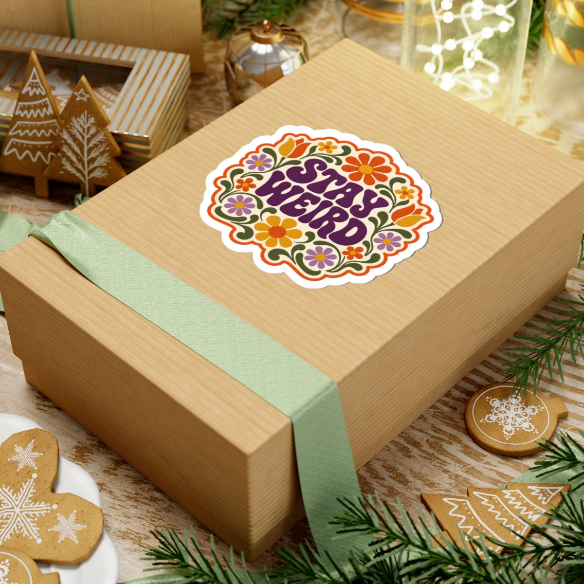 Gift box with a retro "STAY WEIRD" sticker on a festive background with cookies and decorations.