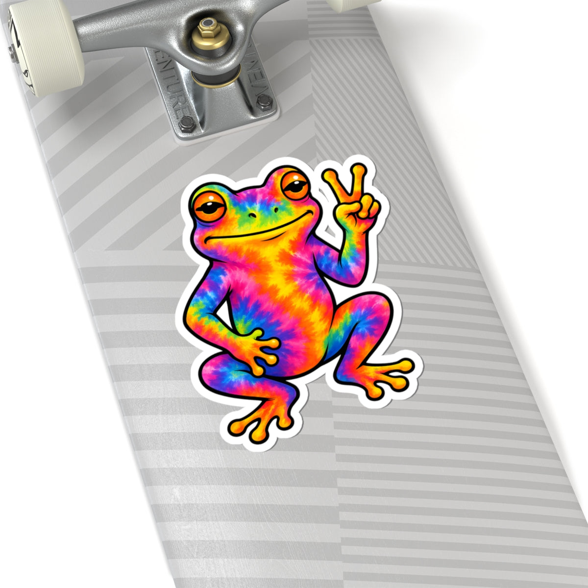 A kiss-cut vinyl sticker of a colorful tie-dye frog making a peace sign, shown applied to the deck of a skateboard.