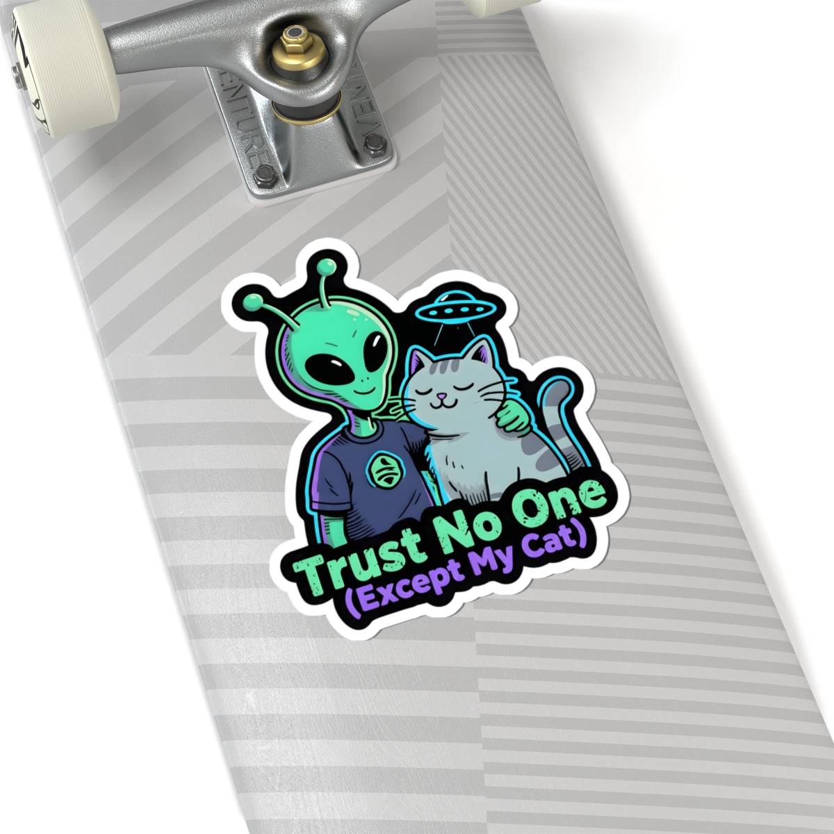 A kiss-cut sticker featuring a green alien hugging a white cat with the text 'Trust No One (Except My Cat)' in neon-style lettering, shown applied to the underside of a skateboard deck.