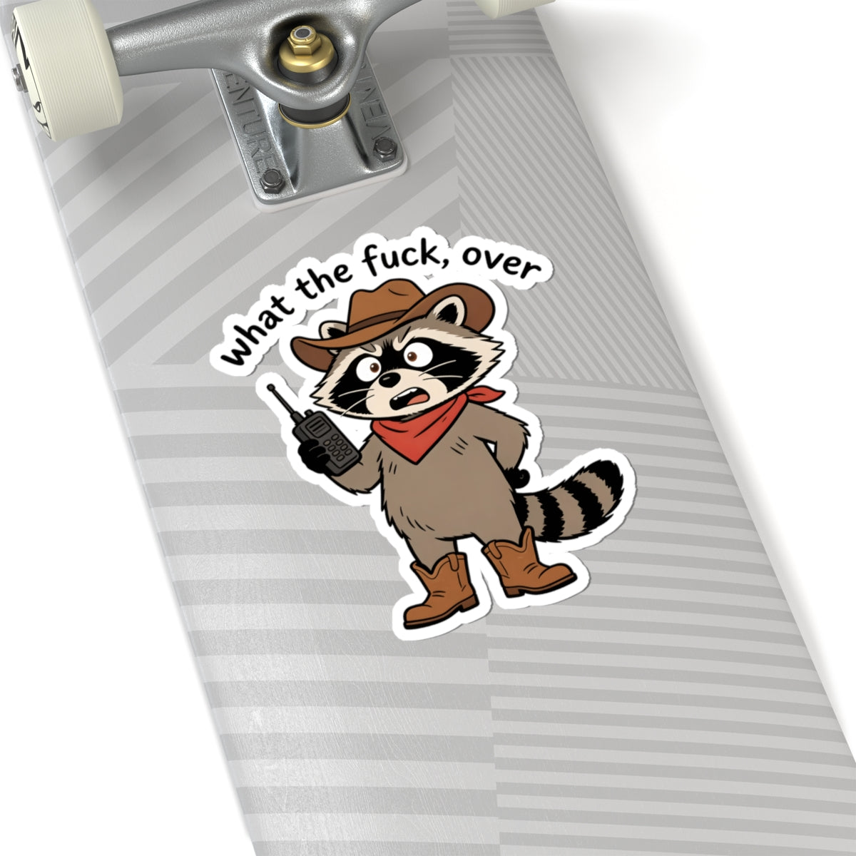 A kiss-cut sticker featuring a cartoon raccoon dressed as a cowboy with the text 'what the fuck, over' applied to a skateboard deck. The skateboard deck has a gray and white striped pattern.