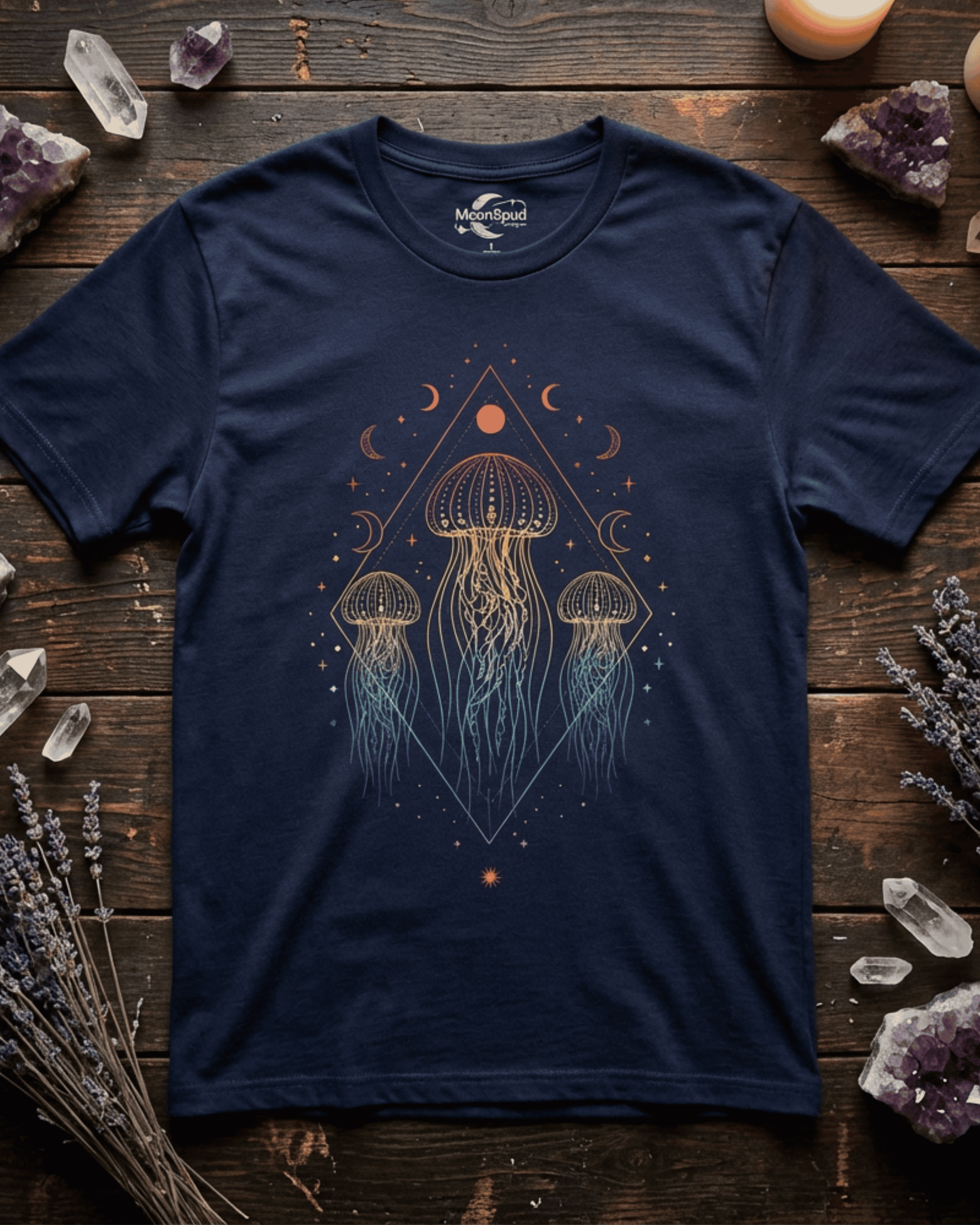 A detailed flatlay of the navy blue Celestial Boho Ocean Lover shirt on a dark wooden table. The shirt's intricate design, featuring a rainbow-colored jellyfish surrounded by celestial moon phases, is beautifully complemented by surrounding amethyst crystals, quartz, and dried lavender.